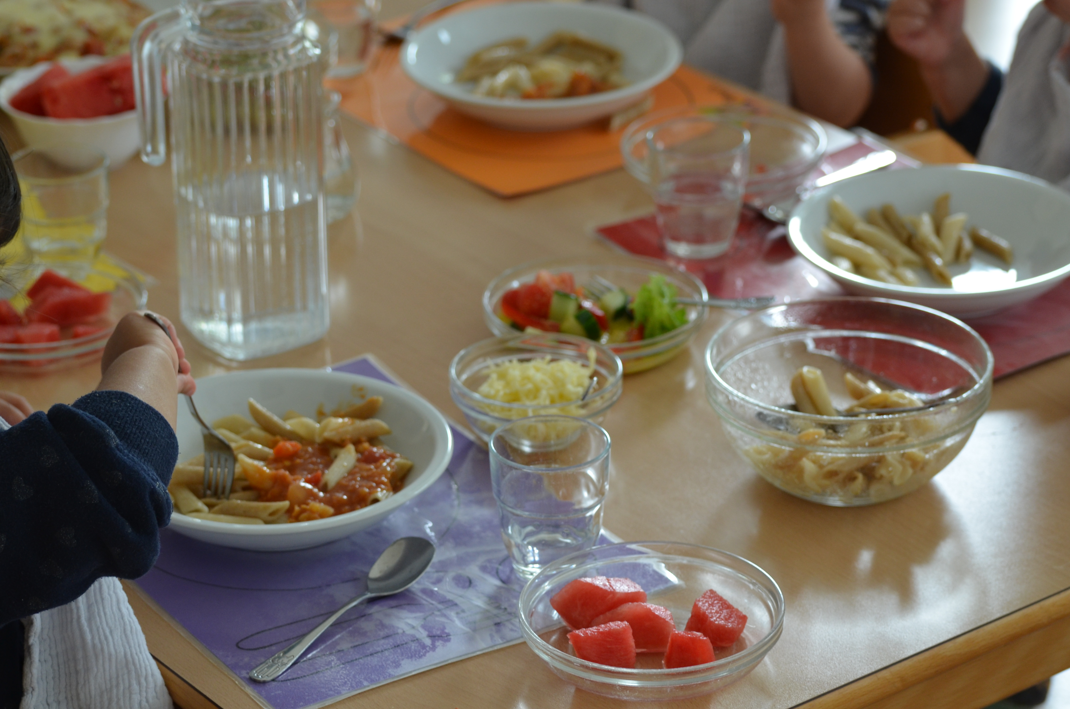 Tisch mit mehreren Tellern voll frischem Essen und Kinderhände mmit Besteck