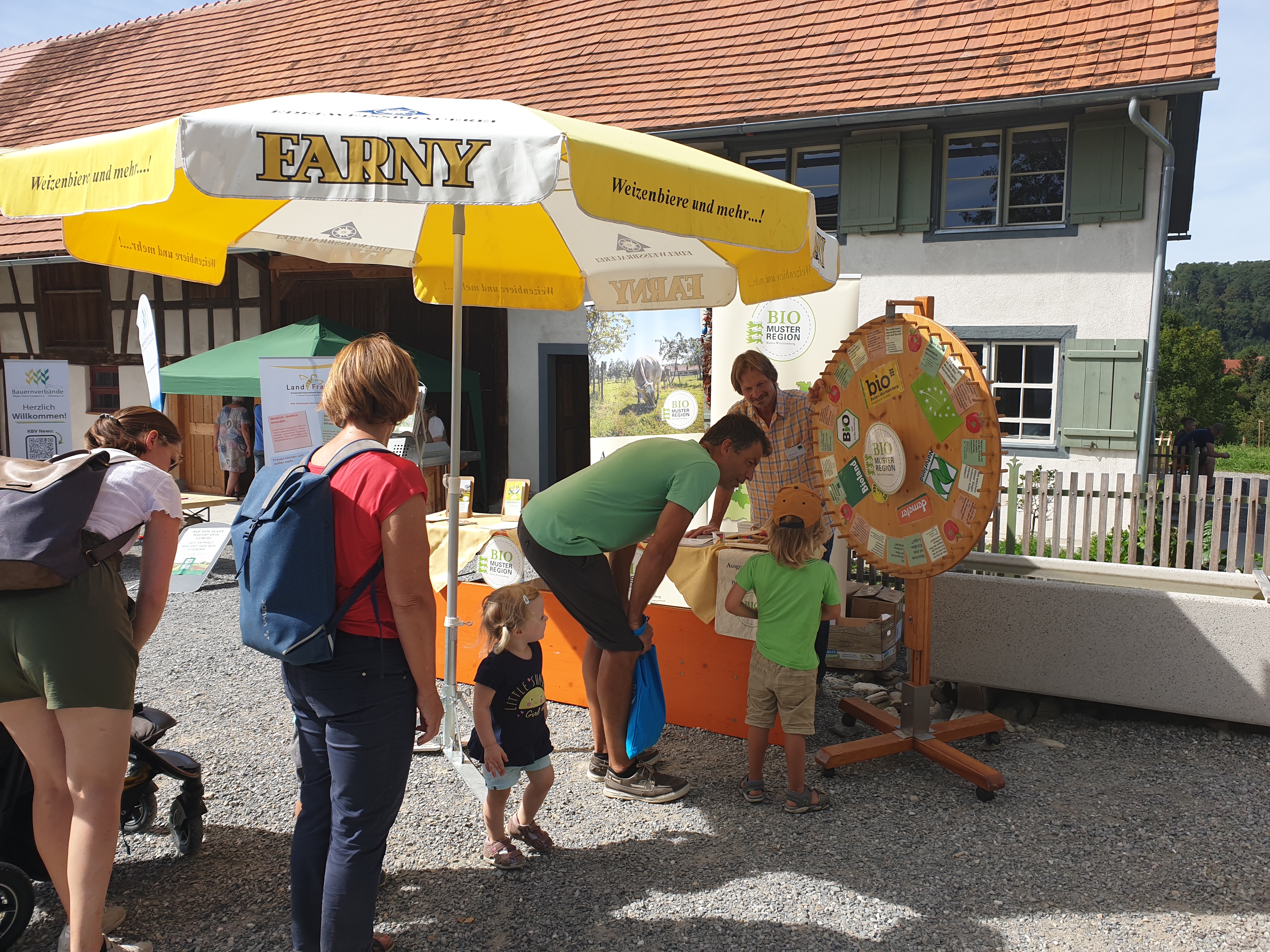 Drei Erwachsene und zwei Kinder stehen am Stand der Bio-Musterregion und drehen am Glücksrad